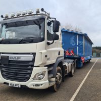 White vehicle moving a static caravan wrapped in blue plastic