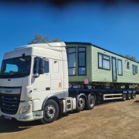White truck carrying a green mobile home on a flatbed