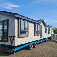 White flatbed vehicle carrying a fancy static caravan